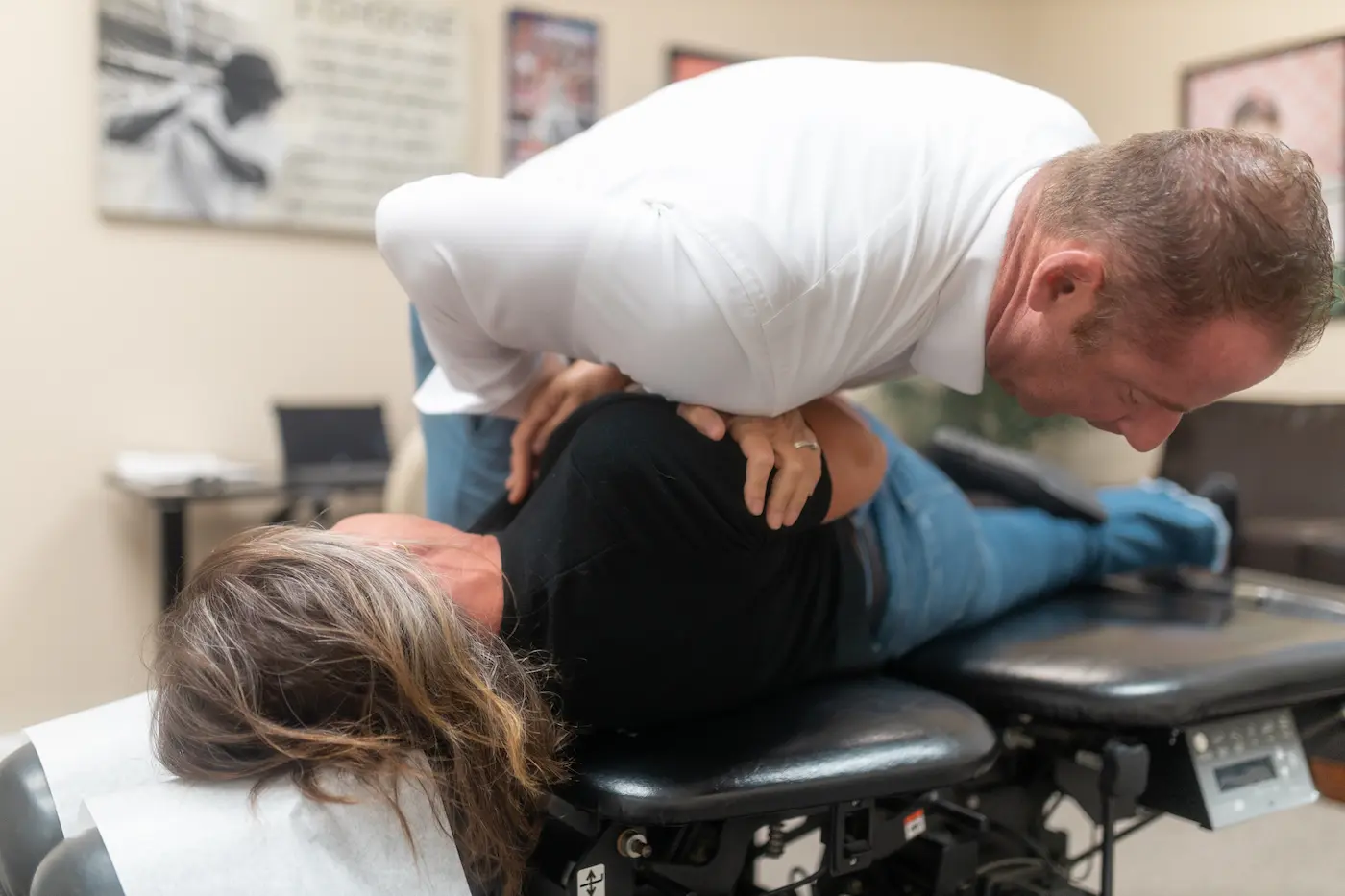 A chiropractor adjusts a patient's upper back on a black treatment table.