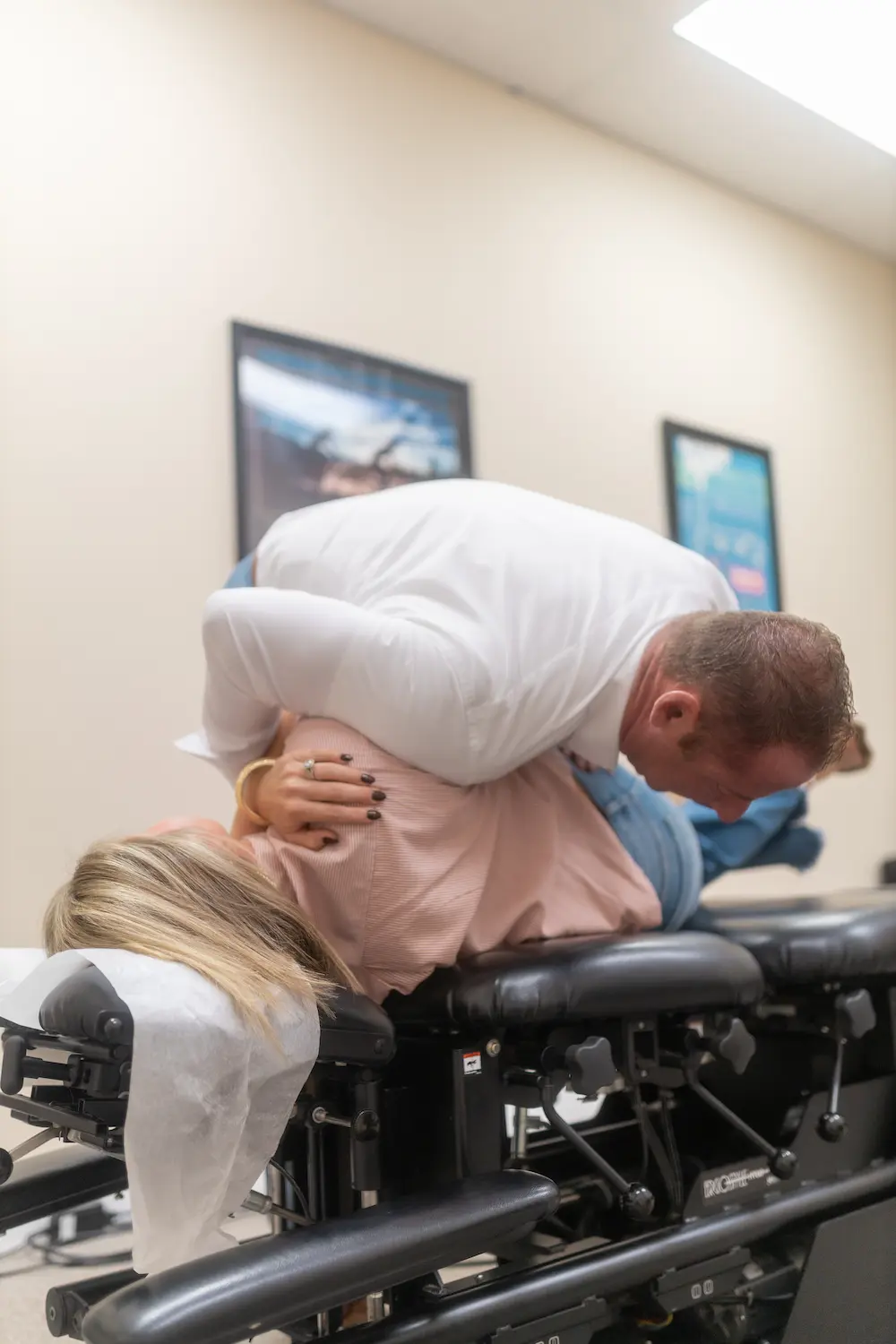 A chiropractor adjusts a female patient lying face down on a black chiropractic table.