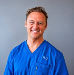 Headshot of a smiling man in blue scrubs with 'Dr. J' embroidered on the chest.