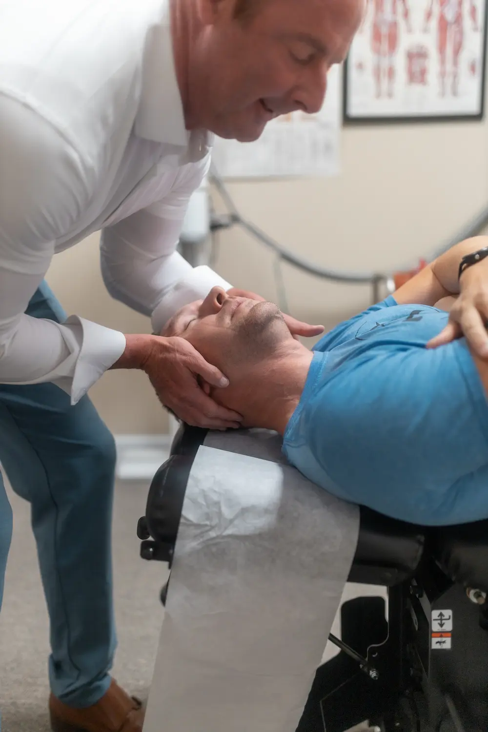 A chiropractor adjusts a patient's neck on an examination table.