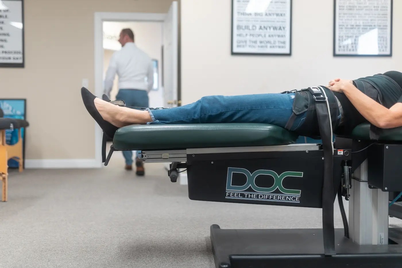 A person lies on a green and black medical table with a harness around their hips, in a clinic setting.