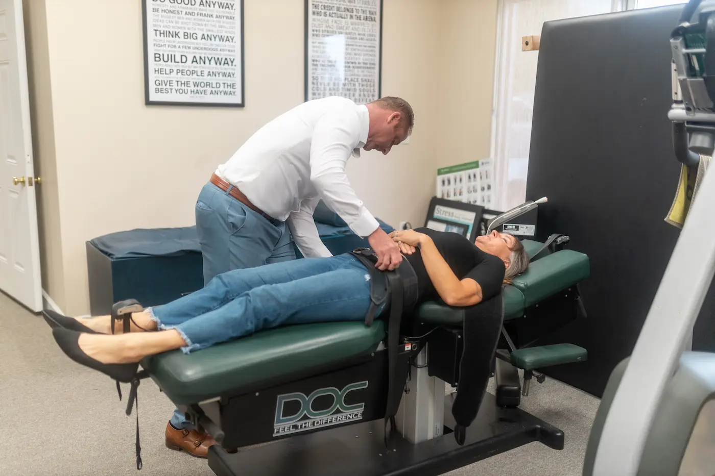 A man in a white shirt adjusts a harness on a woman lying on her back on a chiropractic table.